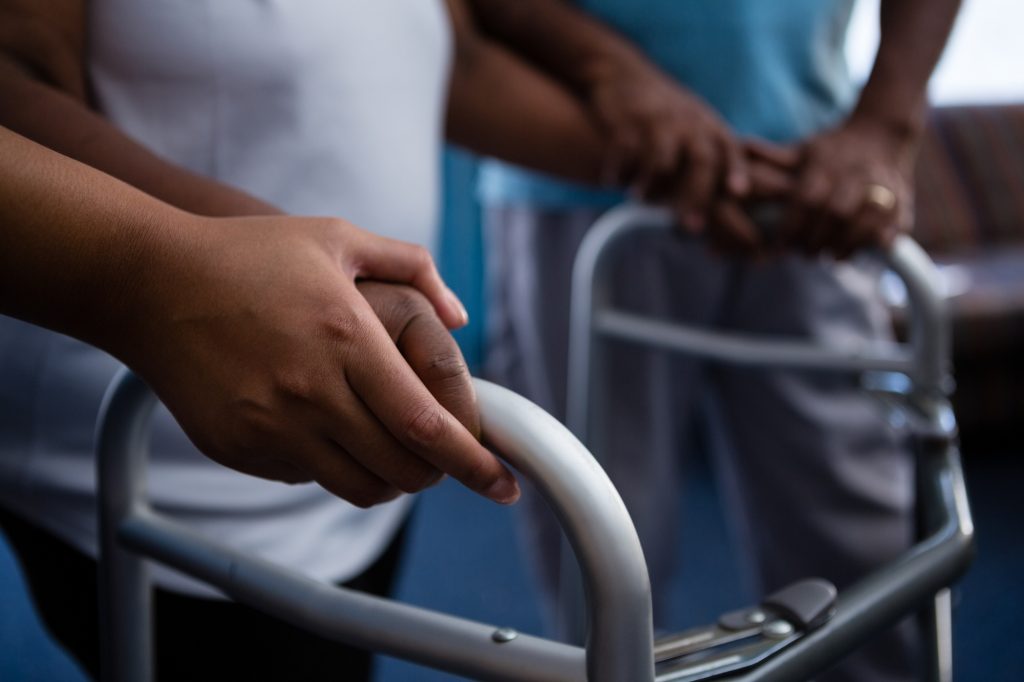 Cropped hands of nurse assisting woman in walking with walker