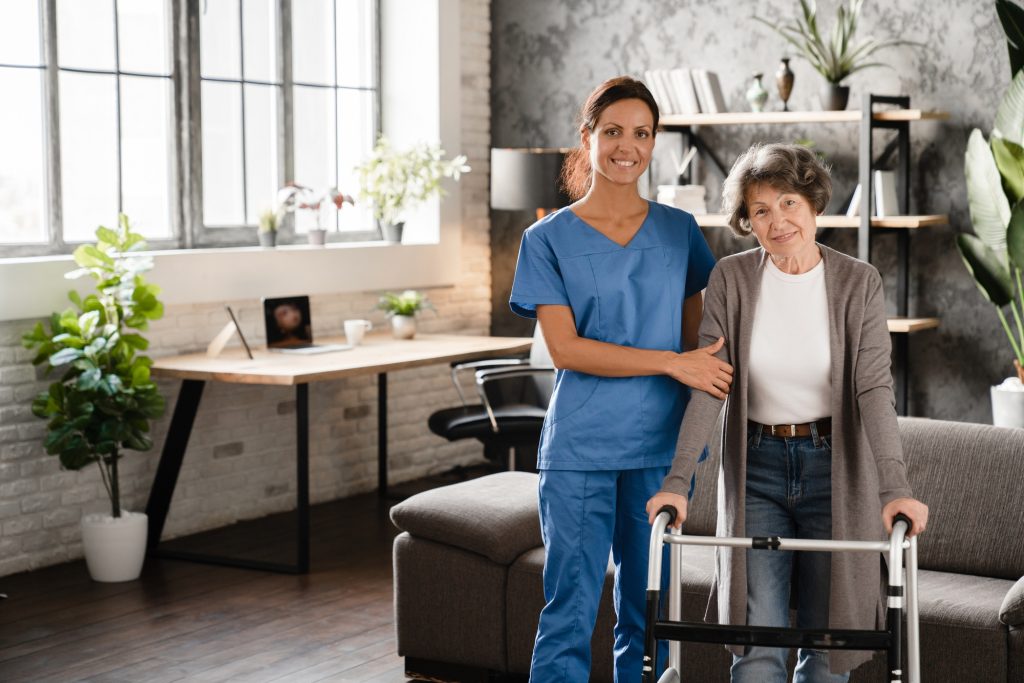 Mature caretaker nurse doctor standing with elderly senior patient grandmother using walking frame